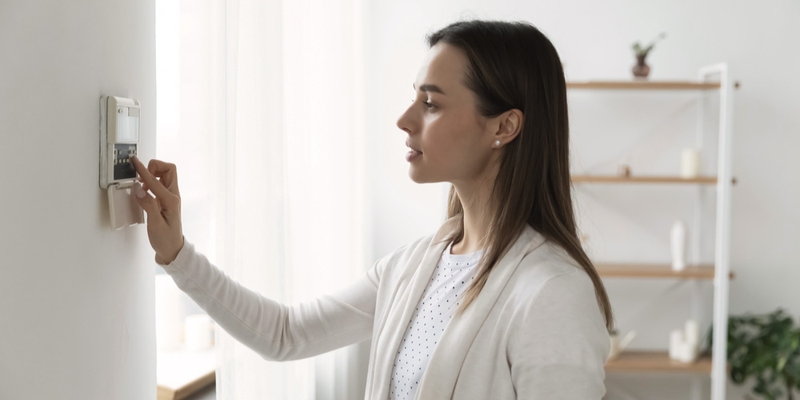 Woman clicks home security system on wall